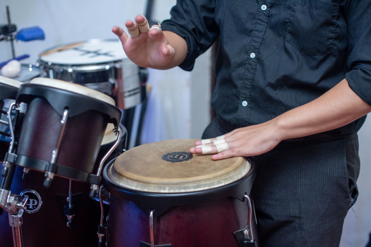 features-03 Close-up of a musician's hands playing congas indoors, highlighting rhythm and percussion.